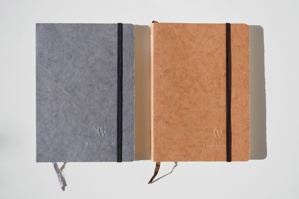 Zwei Clairefontaine My Essentials Notizbücher im A5-Format, eines in Grau und eines in Beige, mit Gummibandverschluss. Im Notizbuch-Test schnitten sie nur mittelmäßig ab, da ihr Design eher schlicht und bieder wirkt.